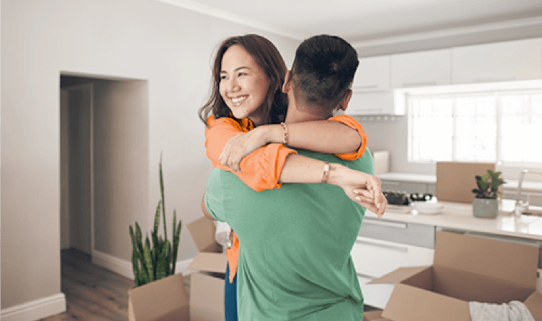 A young couple embracing in the kitchen of a recently purchased home with open moving boxes all around